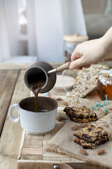 useful breakfast of muesli and dried fruits. Wooden background. A delicious morning. Place for text. Healthy food. Vegetarian. A hand pours coffee into a cup