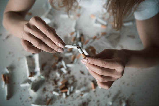 Top view close up of female hands breaking ciggy, shredded cigarettes are lying on table. Focus on coffin nail