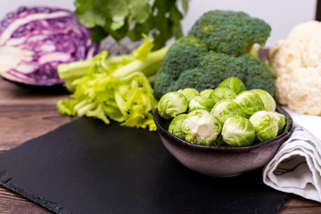 Close up of assorted healthy fresh vegetables on a black slate on a wooden table: cabbage, broccoli, cauliflower and Brussels sprouts and red cabbage