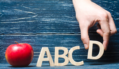 Red apple and letters ABCD. The hand puts the letter D in the alphabet order. Apple for the teacher. The concept of teaching and education. School, college, kindergarten, university. 