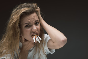 Portrait of depressed woman holding many ciggies with her teeth and looking at camera with disgust....