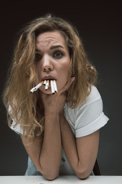 Portrait of discontent girl disliking smoking. She is gulping rollups and holding arms on neck. Isolated on background