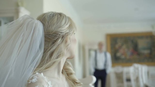 Happy groom comes with smile to smart bride in luxurious apartment
