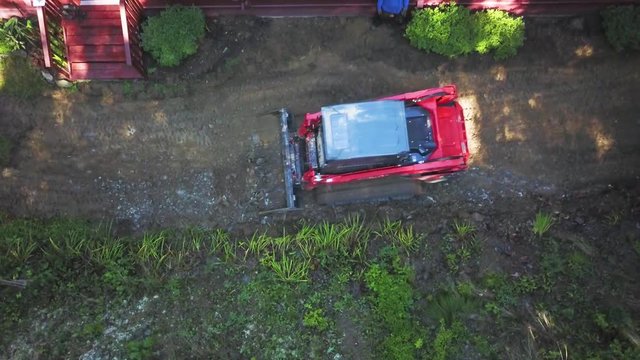 Using a skid steer loader, landscape architect digs a layer of dirt away and makes the existing dirt level.