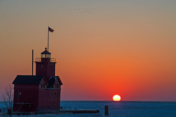 Michigan red lighthouse on Lake Michigan pier in winter at sunset time