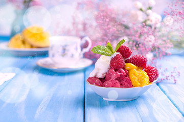 Fruit ice cream with raspberries and mango. Flowers and ripe mango on a blue wooden background. Breakfast is sweet and coffee.