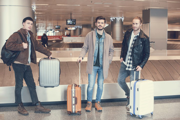 Full length portrait of outgoing male friends standing in airport. Vacation concept