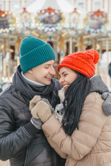 Cheerful smiling caucasian couple of man and woman having fun on european street walk. Casual outfit: jeans, jackets and hats. Winter cold weather with snow. Decorated Christmas tree on a background