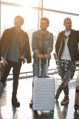 Full length portrait of cheerful comrades standing with baggages in airport. Journey concept
