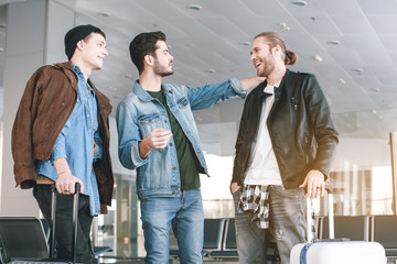 Outgoing friends talking with each other while situating with baggages in airport. Trip concept