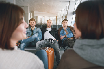 Portrait of cheerful men waiting for plane. Happy male using mobile. Comrades in airport concept