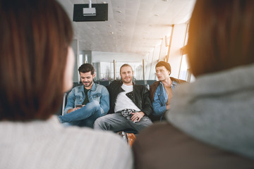 Portrait of smiling young friends sitting in hall. Two people turning back to camera. Expectation...