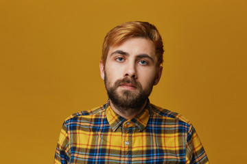 Indoor shot of young bearded male, wears yellow t-shirt listen his girlfriend but feels confused with the words. Isolated over yellow background