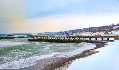 Stormy day at winter beach. Icy waves breaking at snow covered rocks. March 02, 2018. Black sea, Odessa, Ukraine