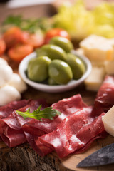 Assorted deli meats and a plate of cheese, on a wooden cutting board. Italian antipasti