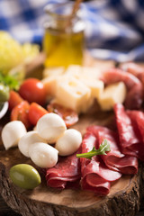 Assorted deli meats and a plate of cheese, on a wooden cutting board. Italian antipasti