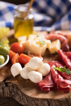 Assorted deli meats and a plate of cheese, on a wooden cutting board. Italian antipasti
