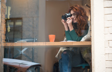 Concentrated girl is photographing street by camera while sitting near window indoors. Copy space