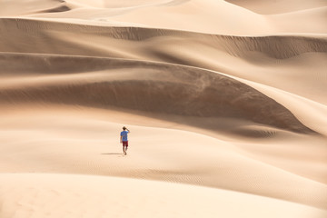 Fototapeta na wymiar Young causasian male tourist in shorts hiking in giant Liwa desert dunes. Abu Dhabi, UAE.
