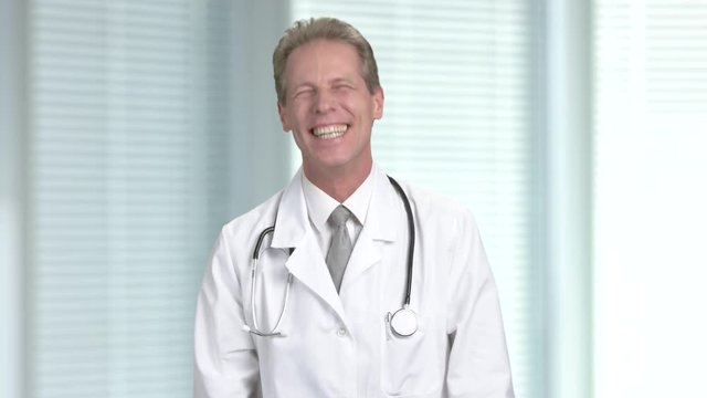 Cheerful doctor on blurred background. Mature male doctor with stethoscope laughing and at hospital.