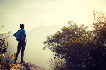 woman backpacker looking at the view on mountain top cliff edge