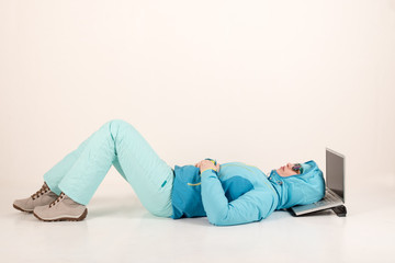 Slender young girl in blue ski suit makes gymnastic exercises in front of a laptop. The concept of sport lifestyle. Busy schedule of young business woman. Sportswear and new computer technologies