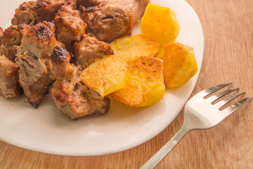 Mutton shish kebabs on two skewers with baked potato on the plate with fork on the wooden table