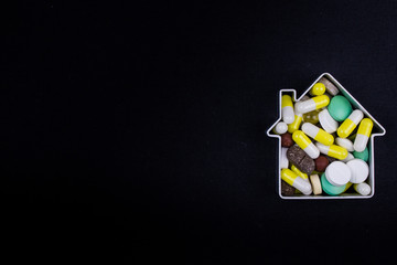 Tablets and capsules in the shape of a house on a dark background. Copy space for text