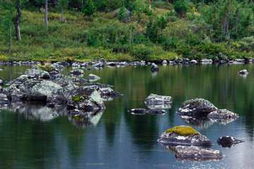 Mountain lake with stones and trees on the shore. Travelling in the mountains.
