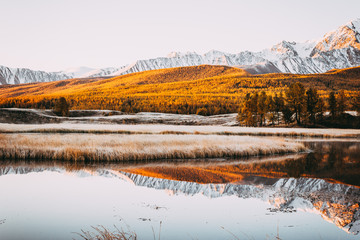Mirror surface and peaks of the rocks of the lake in the mountain valley. The mountain range on the horizon under a colorful sky. Autumn weather