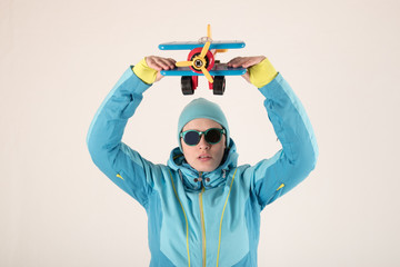 Slender young girl in blue ski suit with toy airplane in her hands posing for sculptor. The concept of sport lifestyle. Busy schedule of young business woman. Collection of sportswear. Pilot style