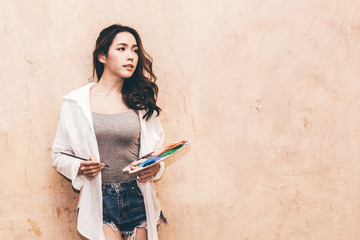 Young woman artist with color palette and watercolor paints on wall background