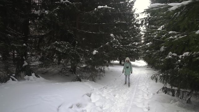 Beautiful young woman in winter clothing, mittens and wool hat photographing snowy forest by a knitted camera