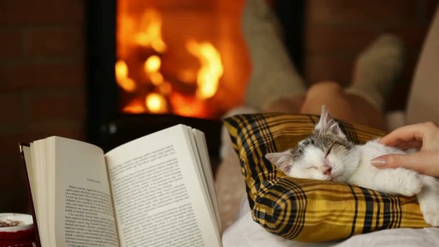 Woman enjoying a good book and fine company - lying by the fireplace reading and cuddling with her kitten