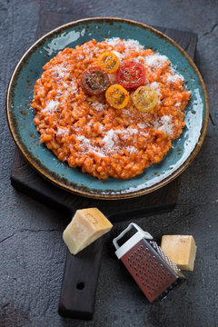 Turquoise plate with tomato risotto and parmesan on a black wooden serving board, vertical shot