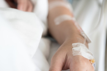 Selective focus on woman patient's hand receiving saline solution by intravenous injection be treated fluid replacement therapy in VIP room in hospital.