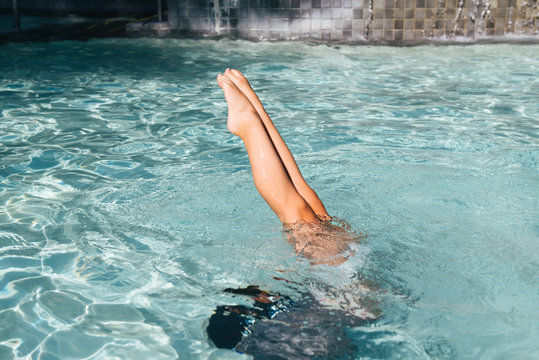 Little girl's legs out of the pool while doing handstand underwater