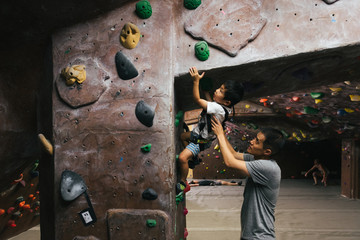 Little boy bouldering in indoor climbing gym with father's help