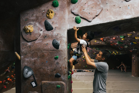 Little boy bouldering in indoor climbing gym with father's help
