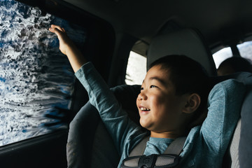 Little Asian boy smiling out car window inside car wash