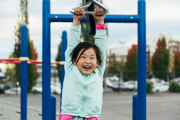 Chinese American girl with large smile rides zip line on playground structure