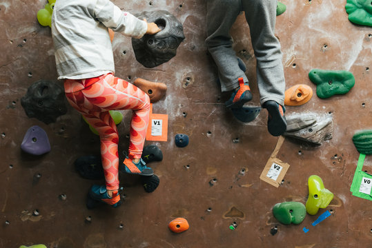 Twin siblings climbing on rock wall next to each other indoors