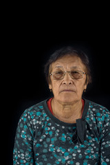 portrait of an elderly woman wearing glasses on a black background.