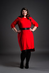 Happy plus size fashion model in red dress, fat woman on gray background, overweight female body