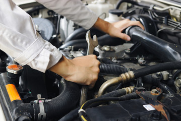 Fototapeta na wymiar Hands of professional mechanic man in white uniform with wrench repairing engine of motor under car hood. Insurance concept.