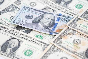 One hundred dollar bill in pile of one dollar banknotes.