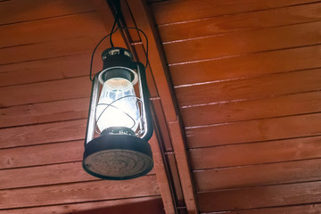 Old kerosene burning lamp hanging on on a wooden ceiling.