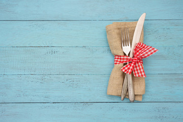 Fork and knife at the napkin with red ribbon on blue wooden board