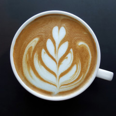 Top view of a mug of latte art coffee on black background.
