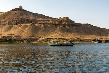 Fototapeta na wymiar Small motor boat for tourists on the Nile River in Cairo (Egypt), in the background ruins of an ancient Arab town in the desert. The tomb of the Aga Khan